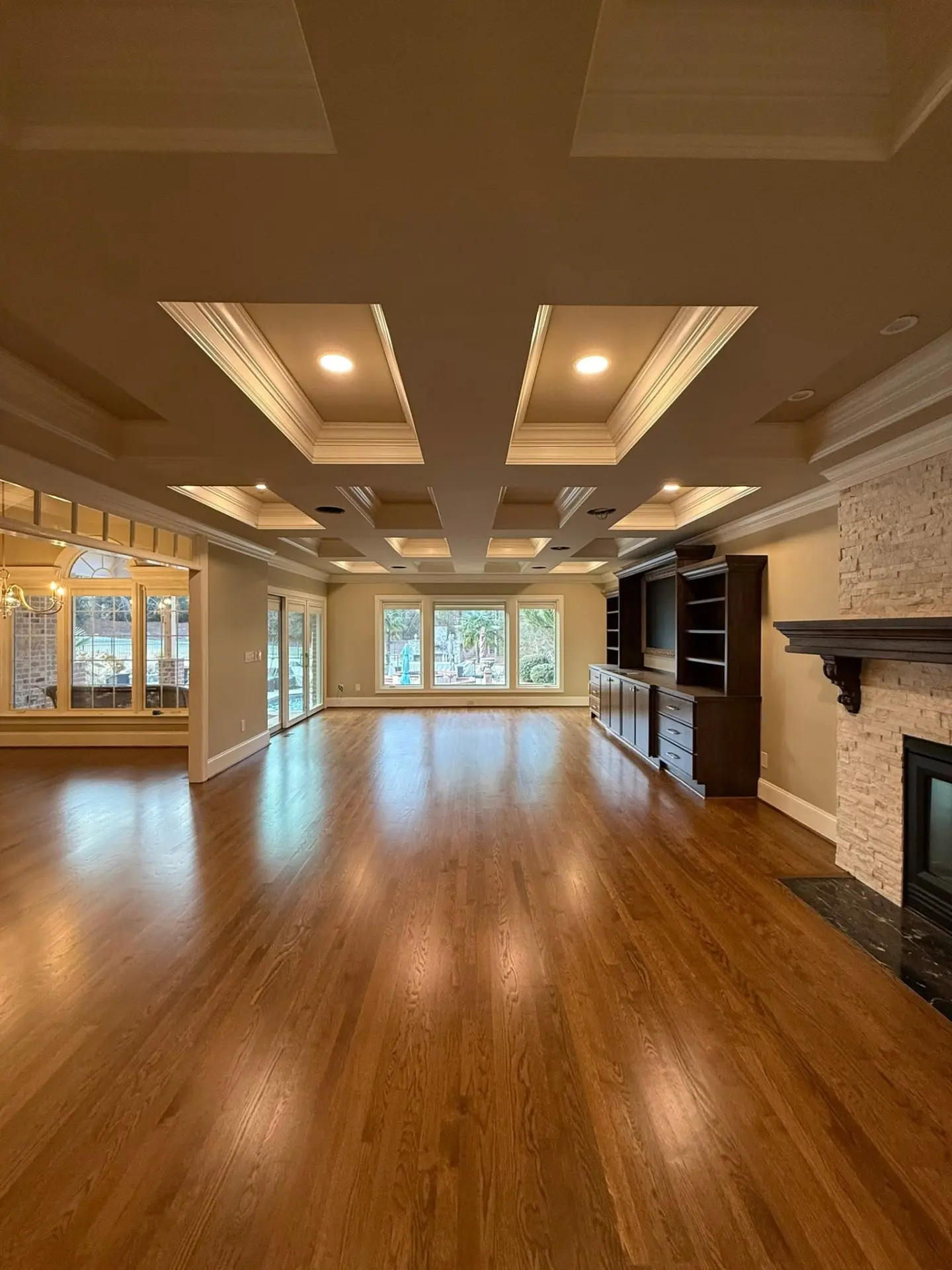 Open-concept great room with coffered ceilings, hardwood floors and stone fireplace built by Woodle Custom Homes